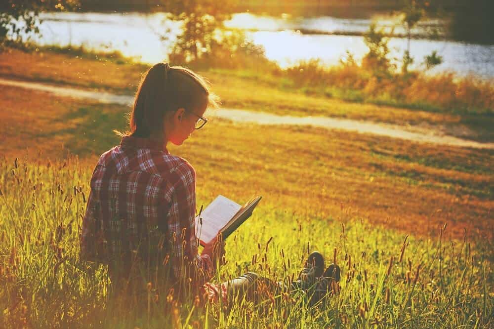 Image of woman in a field sat reading as the sun sets 