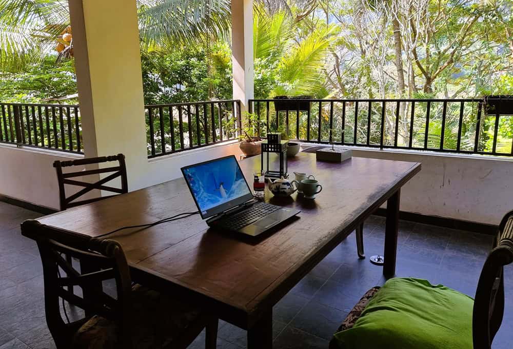 A large wooden table on a veranda surrounded by lush trees   
