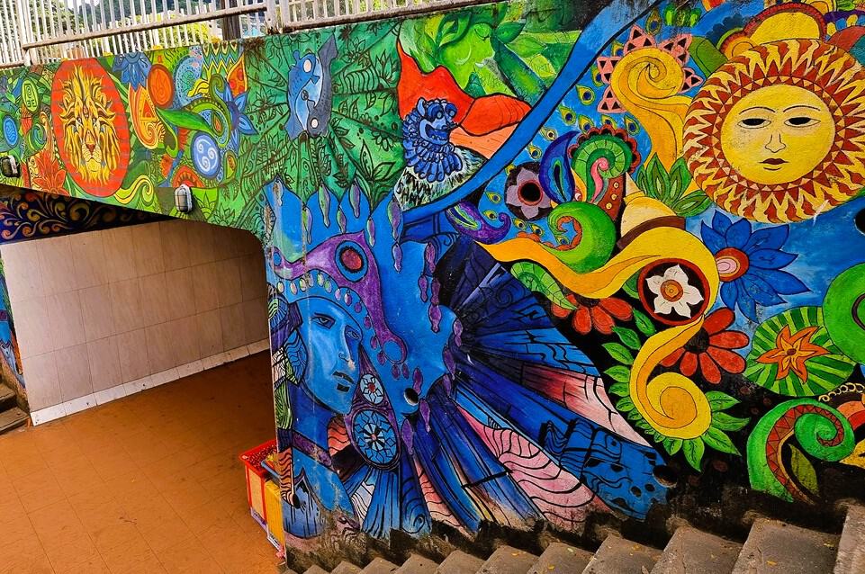 a colourful artistic mural showing a yellow sun, a blue image of a god perhaps, intwined with nature