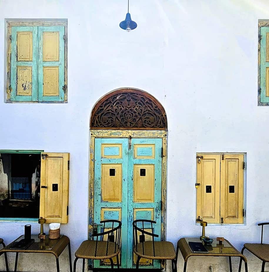 a white building with old colonial style shutters - tables placed outside for coffee