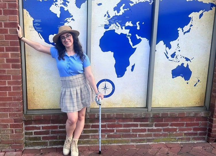 Monica Lynn standing with a cane next to an image of the world 