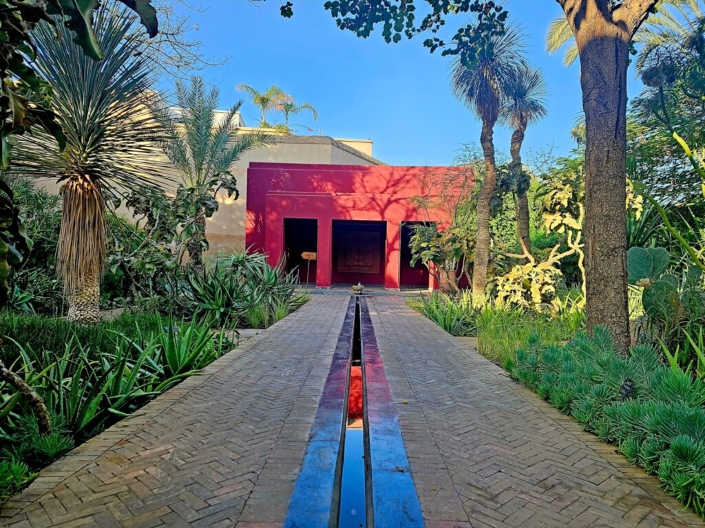 a pathway leading to a red building, amongst tropical trees - Le Jardin Secret - a quite haven for chronic illness solo travellers