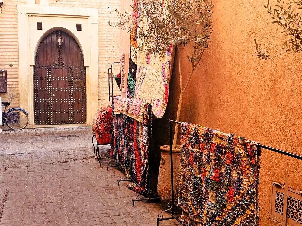 an image of rugs on sale next to pink walls. A large wooden door in the distance 