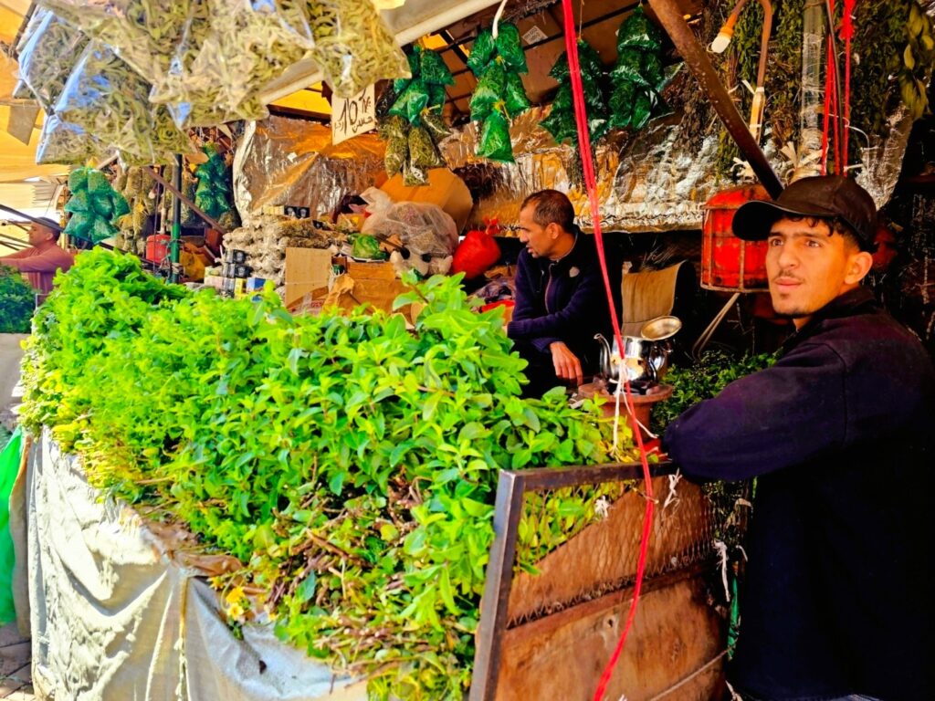 a stall selling a very large heap of mint - with a young man in the foreground looking into the distance 