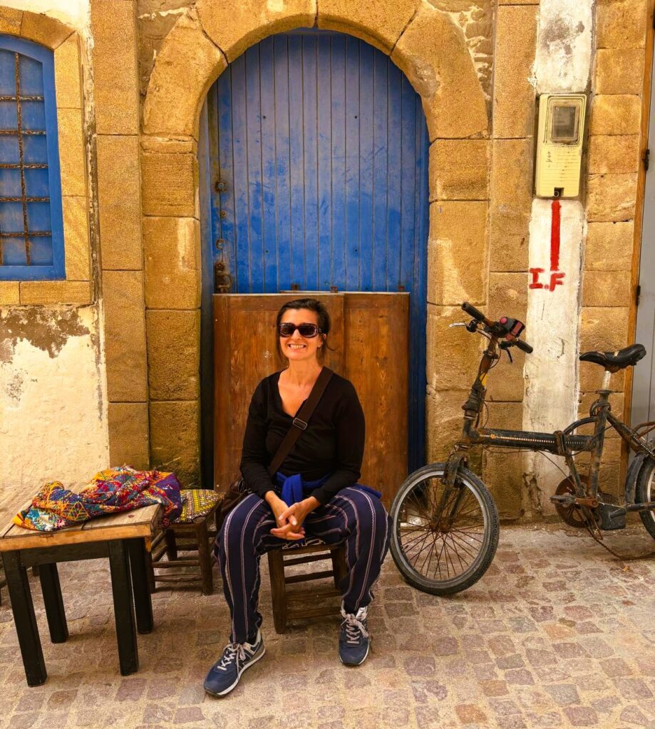 An image of myself sitting next to a table and bike smiling. Happy to be travelling despite a chronic health issue