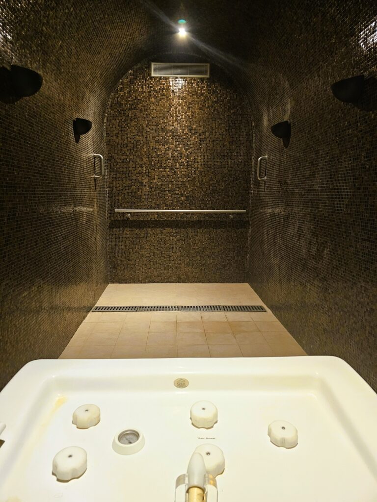 a dark tiled room with a piped jets at one end at Mövenpick Resort & Marine Spa 