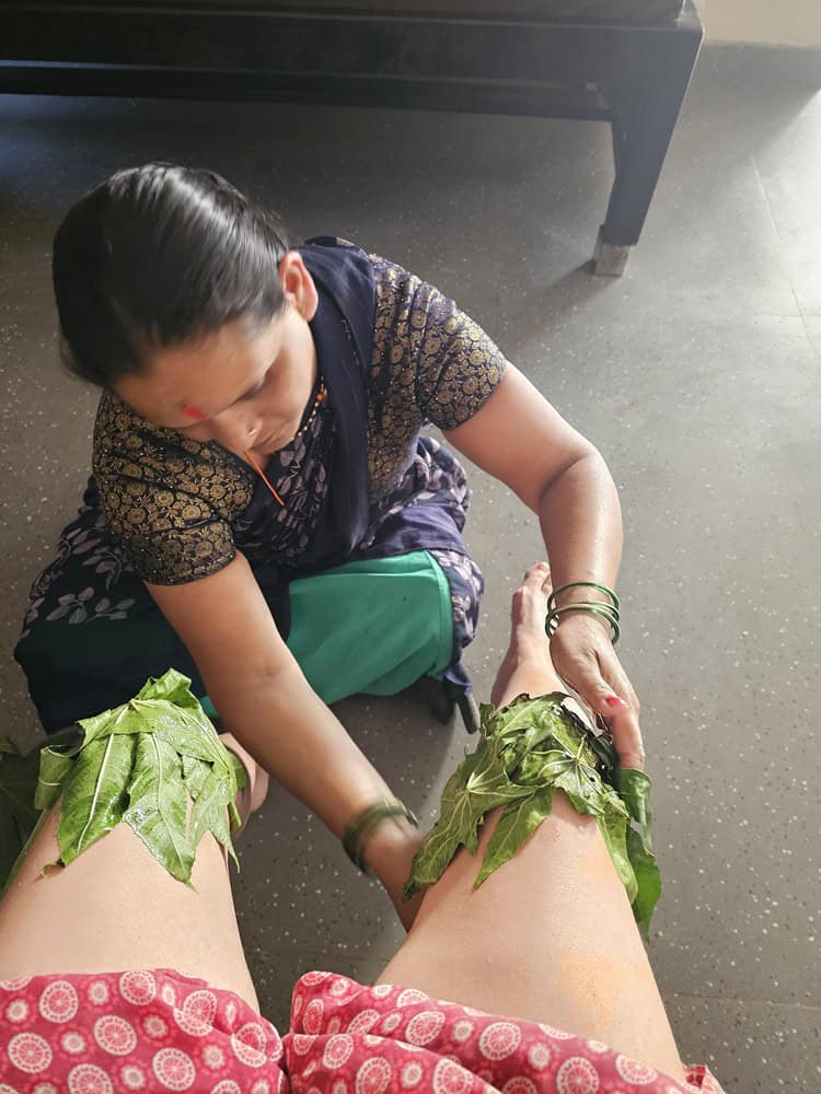 a therapist placing castor leaves on my knees at Nirvana Naturopathy Retreat