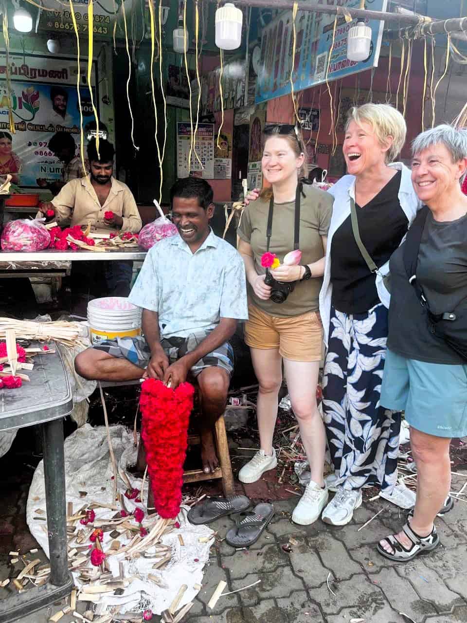 Women at a flower market on SheFarer Women Only Tours in India. SHows two midlife women, one younger woman and a man with flowers