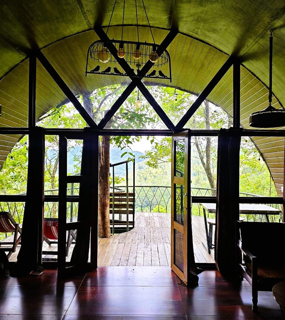 Looking from the cabin through the glass from to the wooden balcony and valley beyond at Tulsi Village Retreat