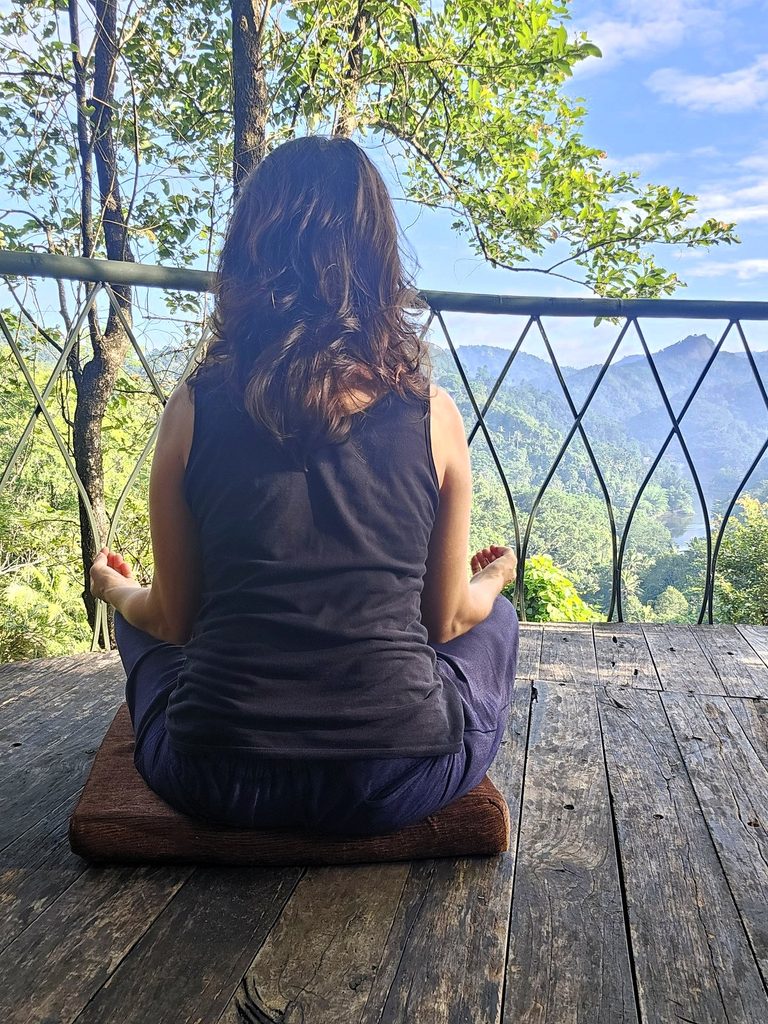 myself from the back sitting crossed legged, looking as though meditating on the balcony at Tulsi Village Retreat in Munnar