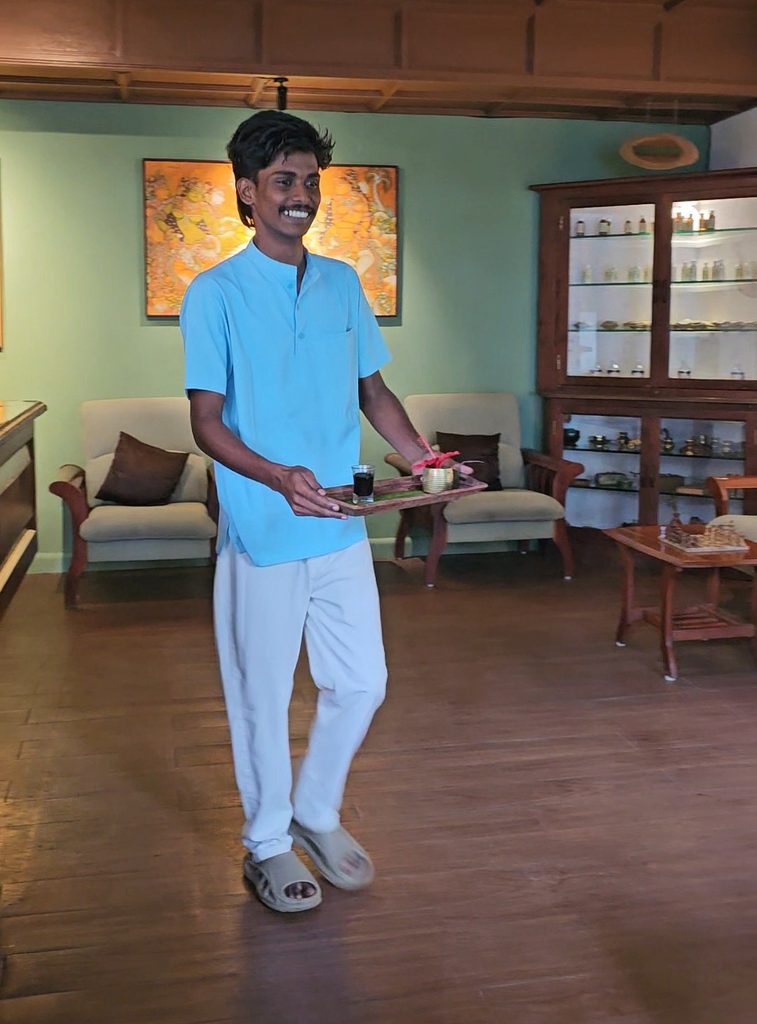 a man who works on reception holding the gooseberry juice on a tray with a flower 