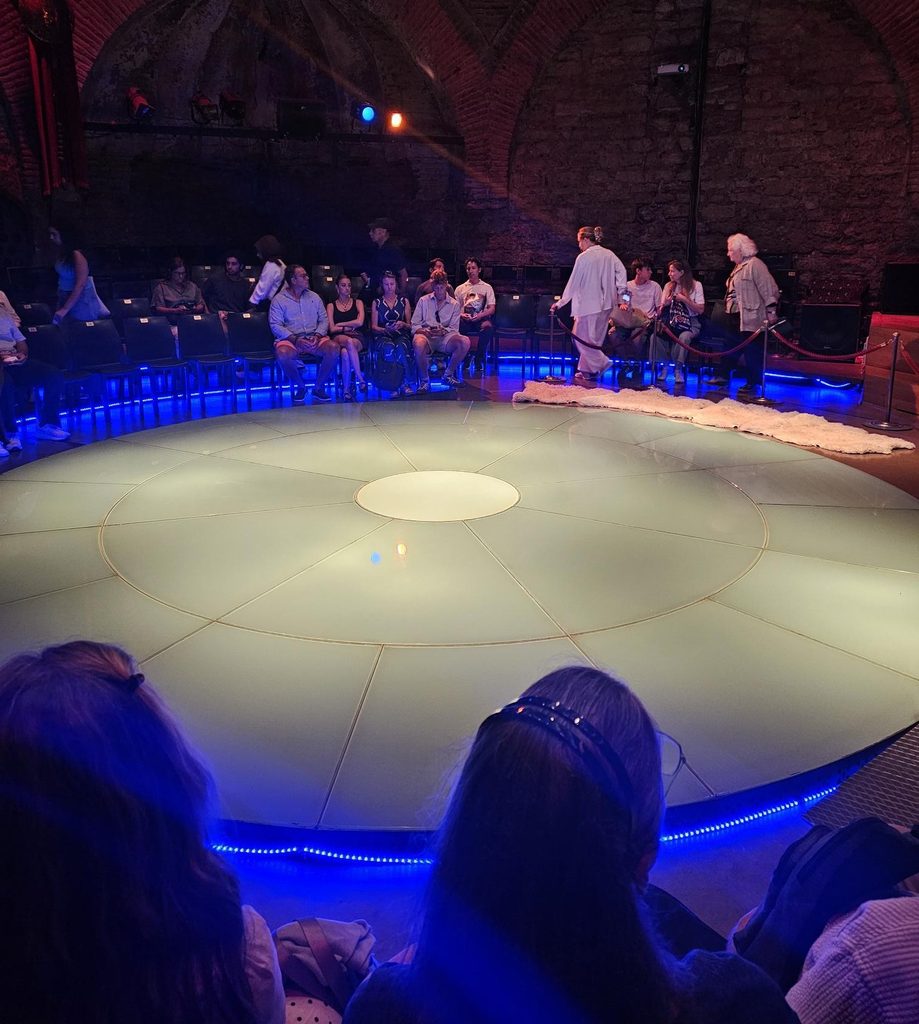 show people entering the area where the stage is - a round performing area lit in white 