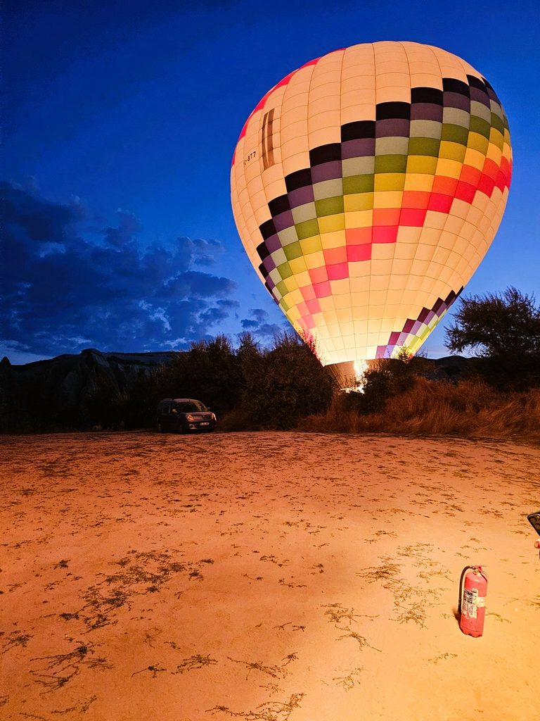 A white hot air balloon with coloured strips glowing in the distance in Cappadocia