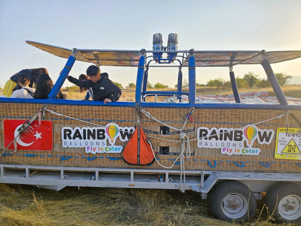 show the basket on the trailer, with a boy climbing out and two people behind. The side says Rainbow Balloons Fly in Colour