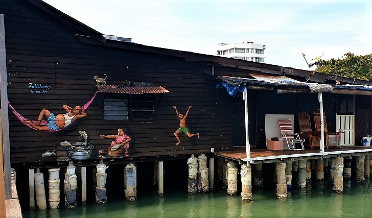 A house on the clan jetty, depicting a mural of man laying in a hammock and two children playing.