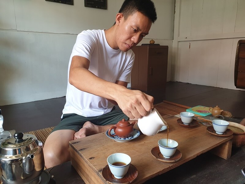 Wilson demonstrates pouring an aged black tea at a low traditional table, sitting on the floor.