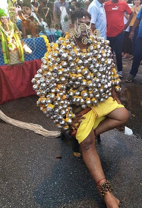 A man with skewers piercing his face and a jacket of silver cups.