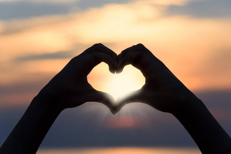 an image of two hands creating a heart shape at sunset