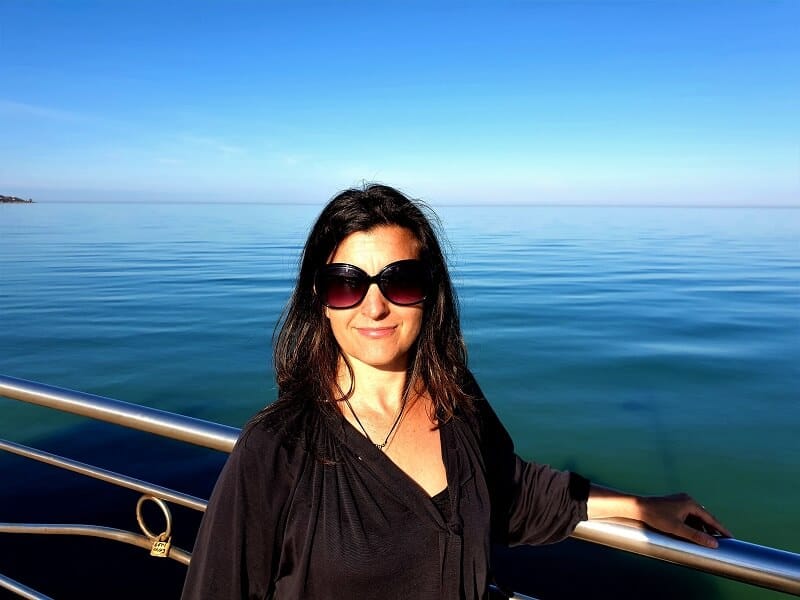 Image of myself standing by the ocean on a warm February day, the colours are vivid blue and I am wearing sunglasses 