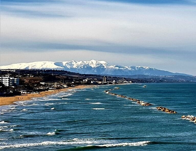 A view of snow capped mountains in the distance, taken from the beach at Termoli