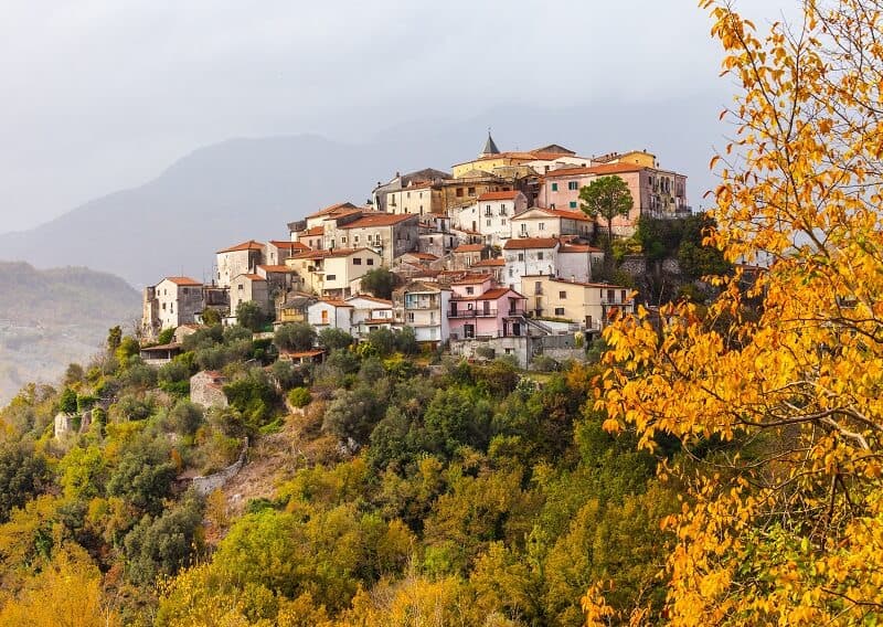 image of a hilltop town, with pastel coloured buildings surrounded by autumnal trees 