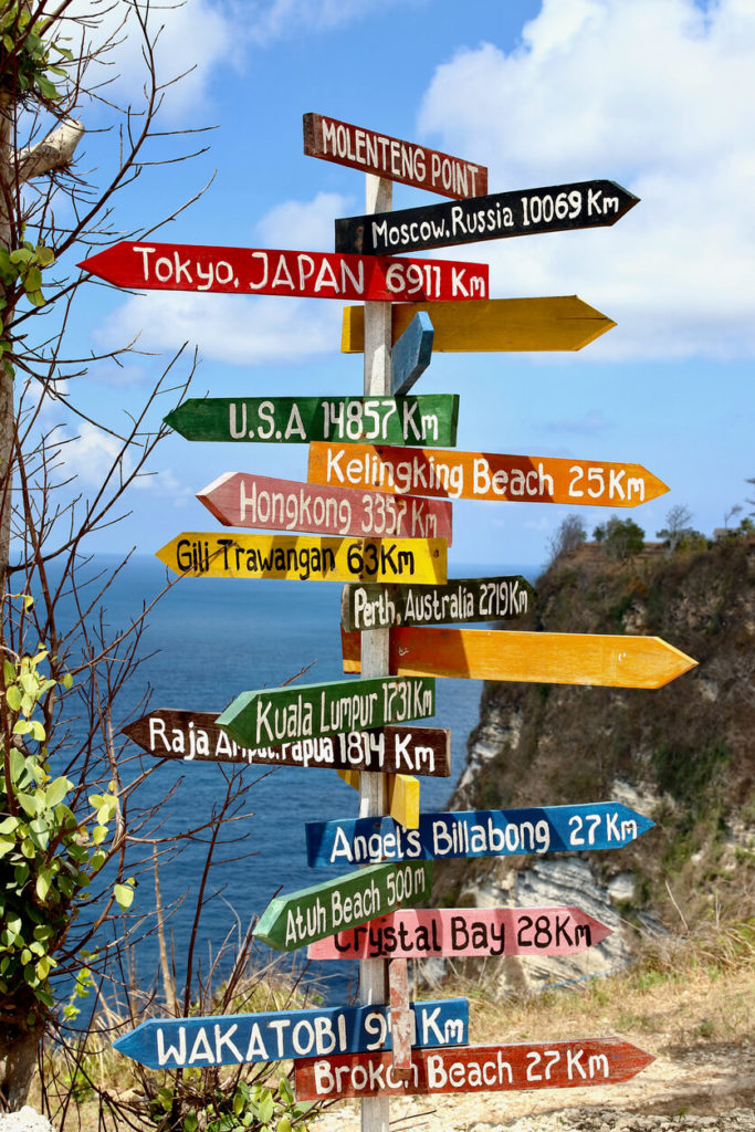 A sign next to the sea with many place names including Kuala Lumpa, Hong Kong, Tokya, Crystal Bay