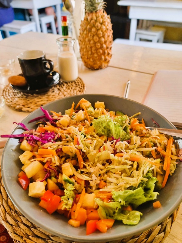 A bowl of mixed salad in the fore front, an espresso cup and pineapple in the background