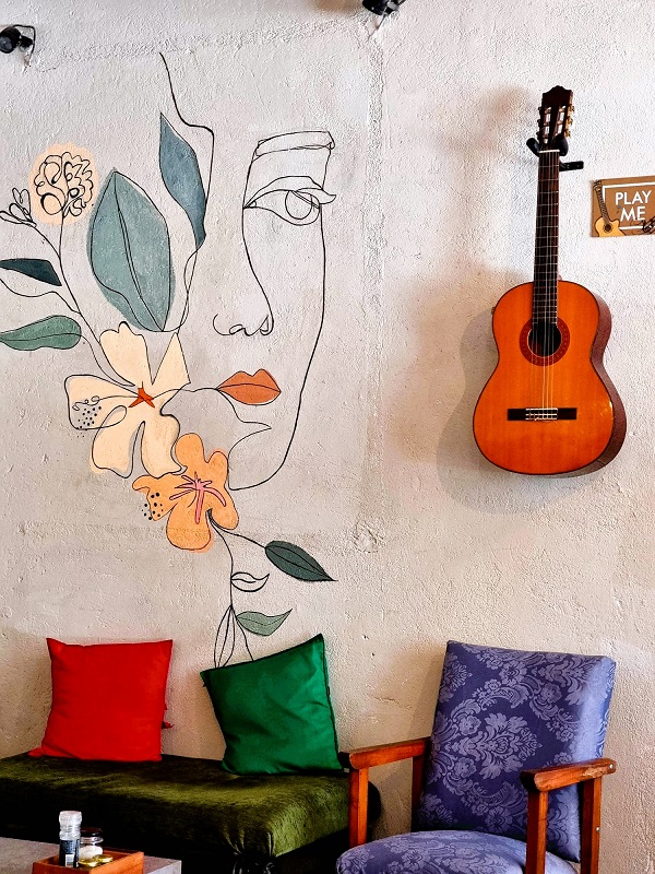 Photo of a wall, ladies profile with flowers painted on it. A guitar. Interior of Buono