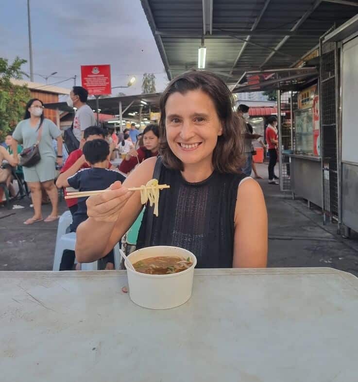 Jenny smiling into the camera eating a bowl of laksa