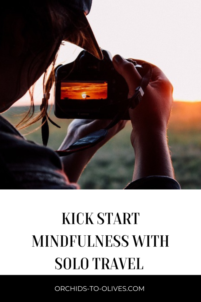 Pinterest - image of a woman holding a camera at a sunset with the title Kick Start Mindfulness With Solo Travel