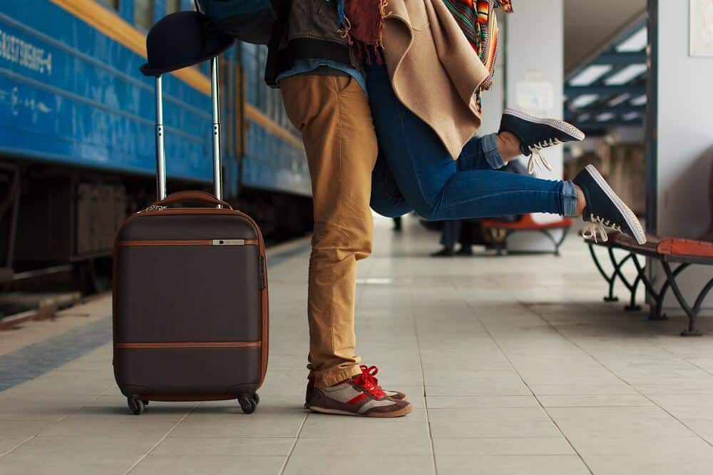 man picking up a woman to embrace next to a train with a suitcase