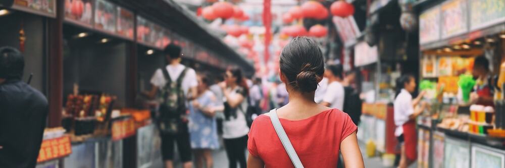 Image of a woman wearing red tee shirt  from behind walking through an Asian market 